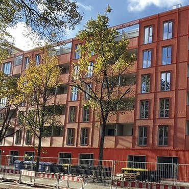 orange-farbener großer Neubau mit grünen Straßenbäumen