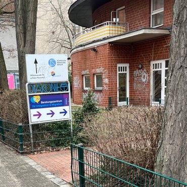 Teil eines Weges mit lila Hinweisschild, das mit Pfeilen die zum Eingang der Beratungsangebots zeigt